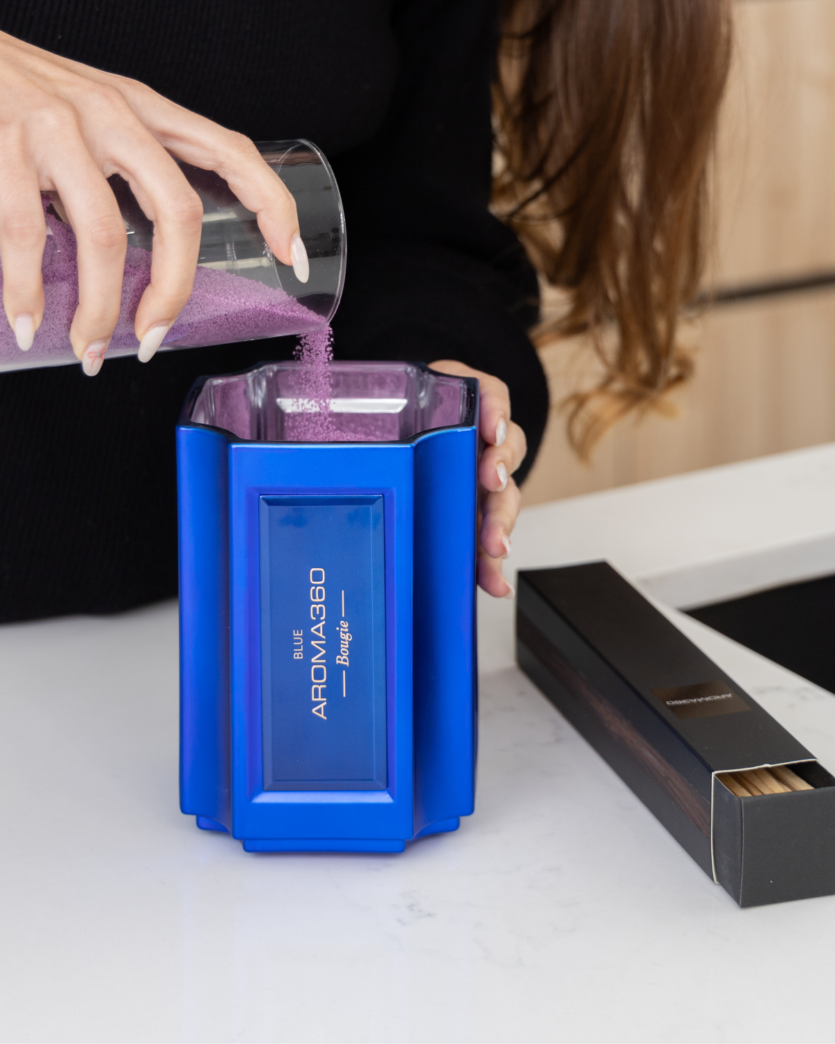 The Bougie Sand Wax Set features a 40oz scented sand wax, 30 candle wicks, and a stunning 33oz recyclable metallic vessel. Available in Blue, Red, Black, Green, and Purple scents, this eco-friendly, refillable candle set offers a sustainable and opulent ambiance.